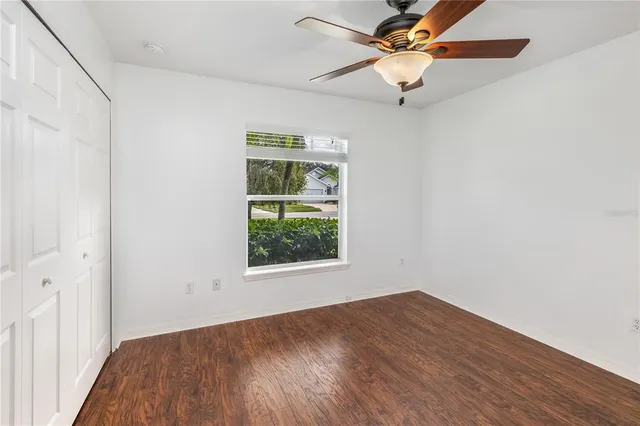 an empty room with wooden floor fan and windows