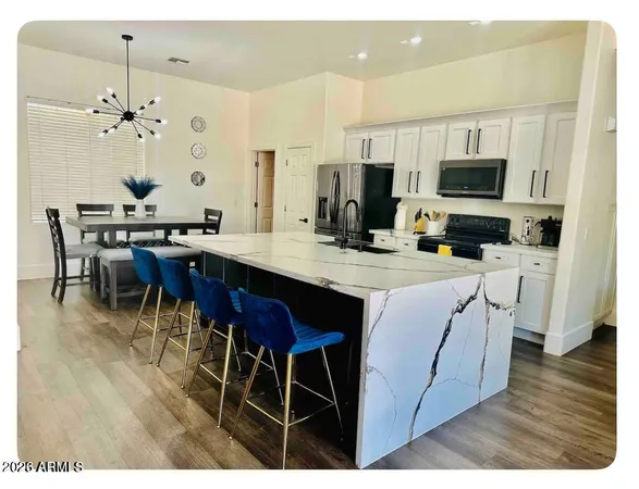 a kitchen with stainless steel appliances kitchen island granite countertop a sink dishwasher a microwave oven a stove with white cabinets and wooden floor