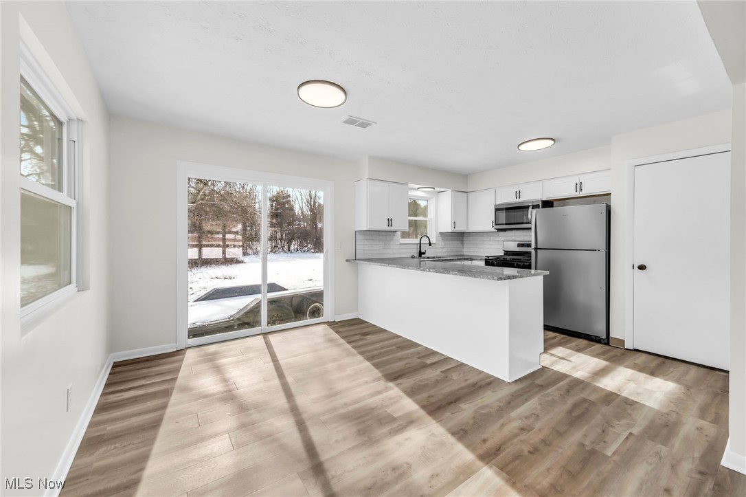 Kitchen featuring stainless steel appliances, dark stone countertops, white cabinetry, a peninsula, and light wood finished floors