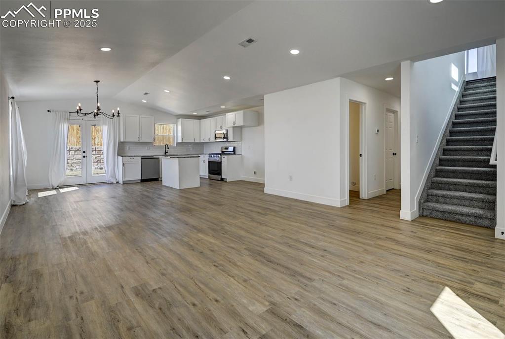1436 Brewery Road Pueblo, CO 81001 - Photo 4 of 40 Unfurnished living room featuring stairway, vaulted ceiling, visible vents, a notable chandelier, and wood finished floors