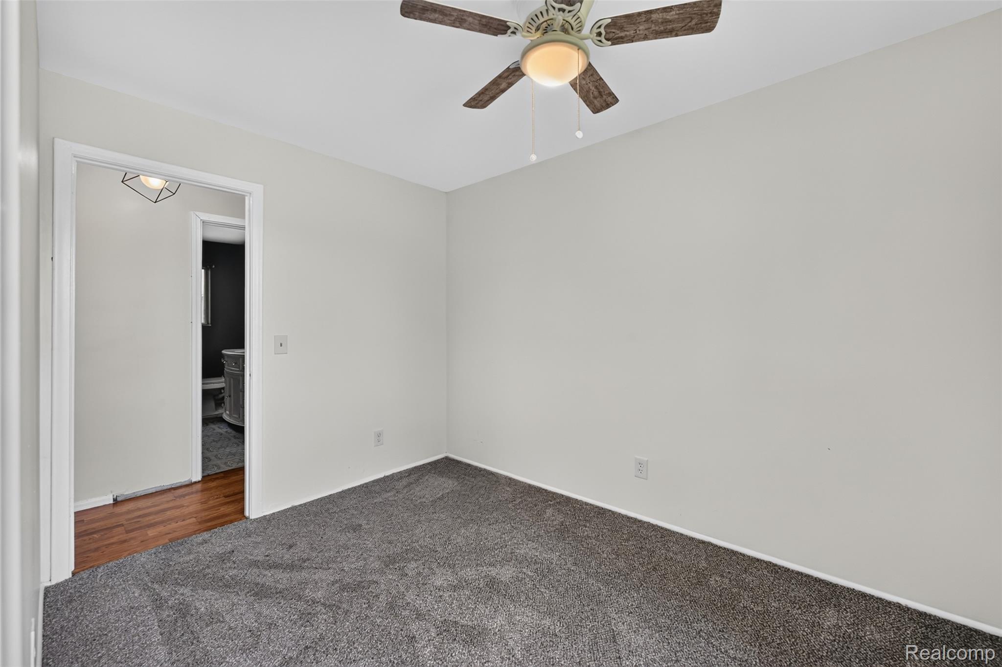 5457 Reid Road Swartz Creek, MI 48473 - Photo 28 of 51 Carpeted room featuring a ceiling fan with integrated lighting, neutral wall tones, and a doorway revealing wood-finish flooring and a vanity