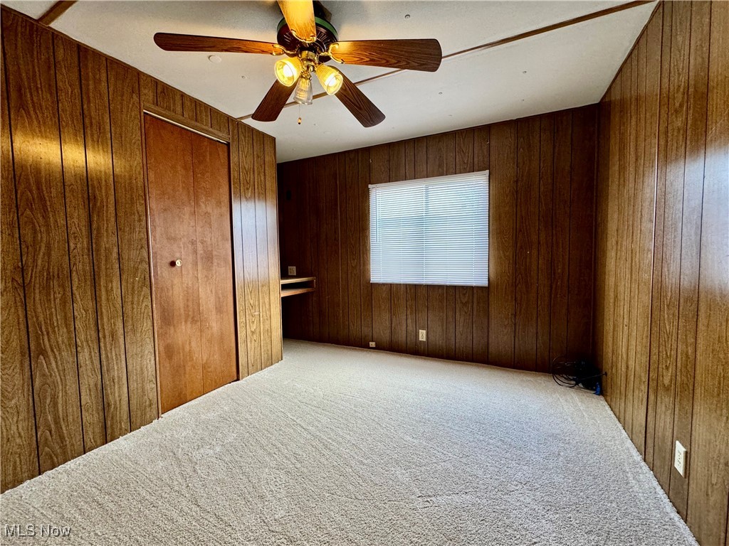 4199 Massillon Road, Unit 11 Uniontown, OH 44685 - Photo 8 of 10 Unfurnished bedroom featuring carpet flooring, a closet, ceiling fan, and wooden walls