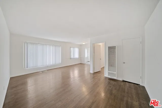a view of an empty room with wooden floor and window