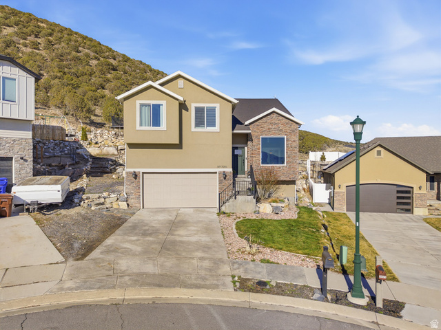 7001 Southpass Road Eagle Mountain, UT 84005 - Photo 1 of 1 View of front of property featuring driveway, stucco siding, a garage, a mountain view, and stone siding