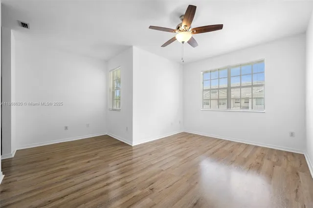 an empty room with wooden floor fan and windows