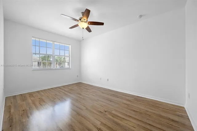 an empty room with wooden floor fan and windows