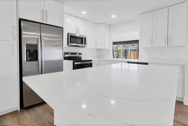 a large white kitchen with stainless steel appliances a refrigerator a stove a microwave and cabinets