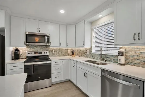 a kitchen with white cabinets appliances a sink and a window
