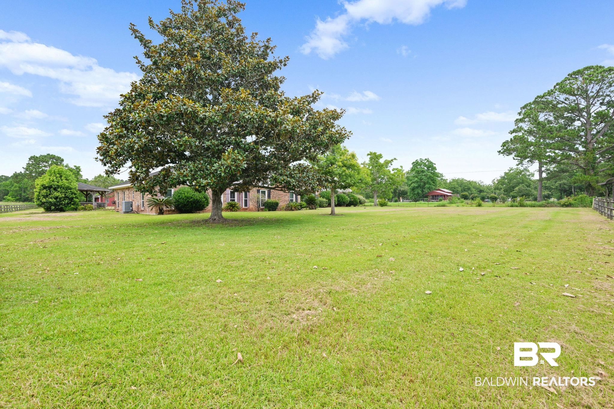 7540 2 Mile Road Irvington, AL 36544 - Photo 70 of 82 Expansive green lawn with mature trees, brick exterior residence, covered porch, and partial fencing