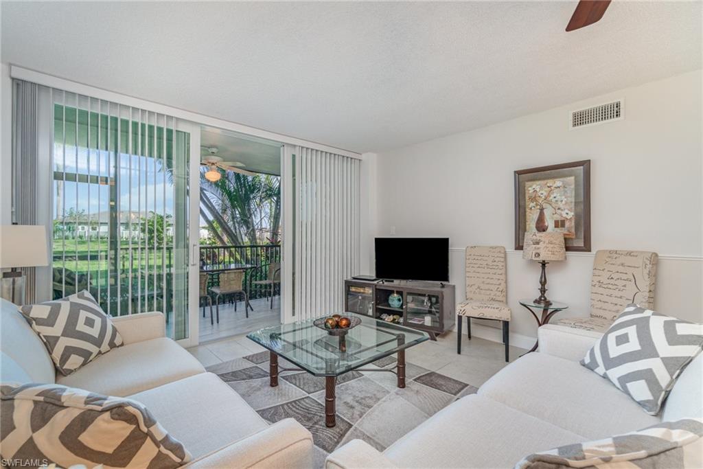 25806 Cockleshell Drive, Unit 115 Bonita Springs, FL 34135 - Photo 2 of 25 a living room with furniture a flat screen tv and a floor to ceiling window