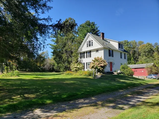 a view of a white house in front of a big yard with plants and wooden fence