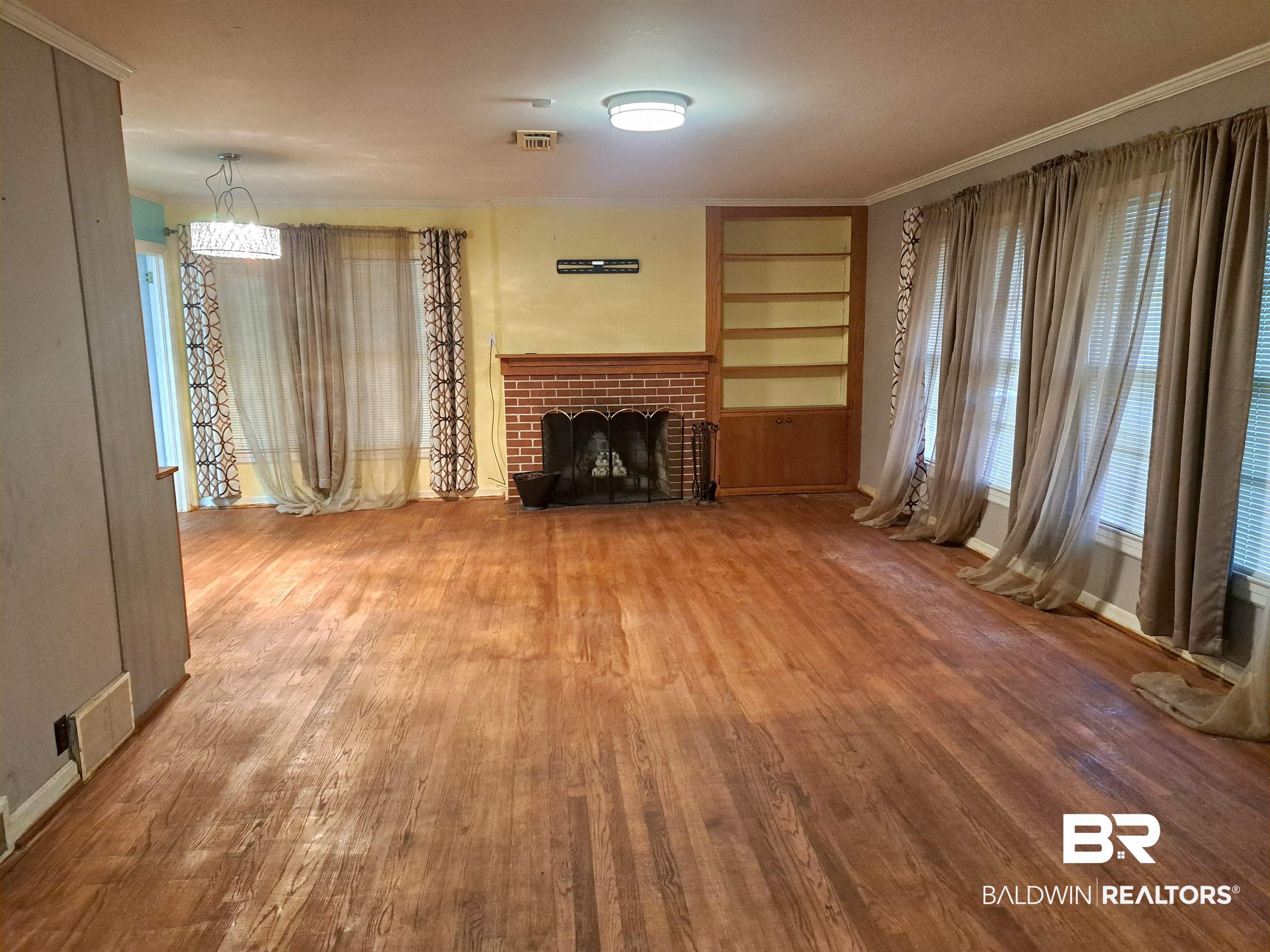 249 Newton Parkway Evergreen, AL 36401 - Photo 3 of 28 Unfurnished living room featuring built in shelves, wood-type flooring, a brick fireplace, and healthy amount of natural light