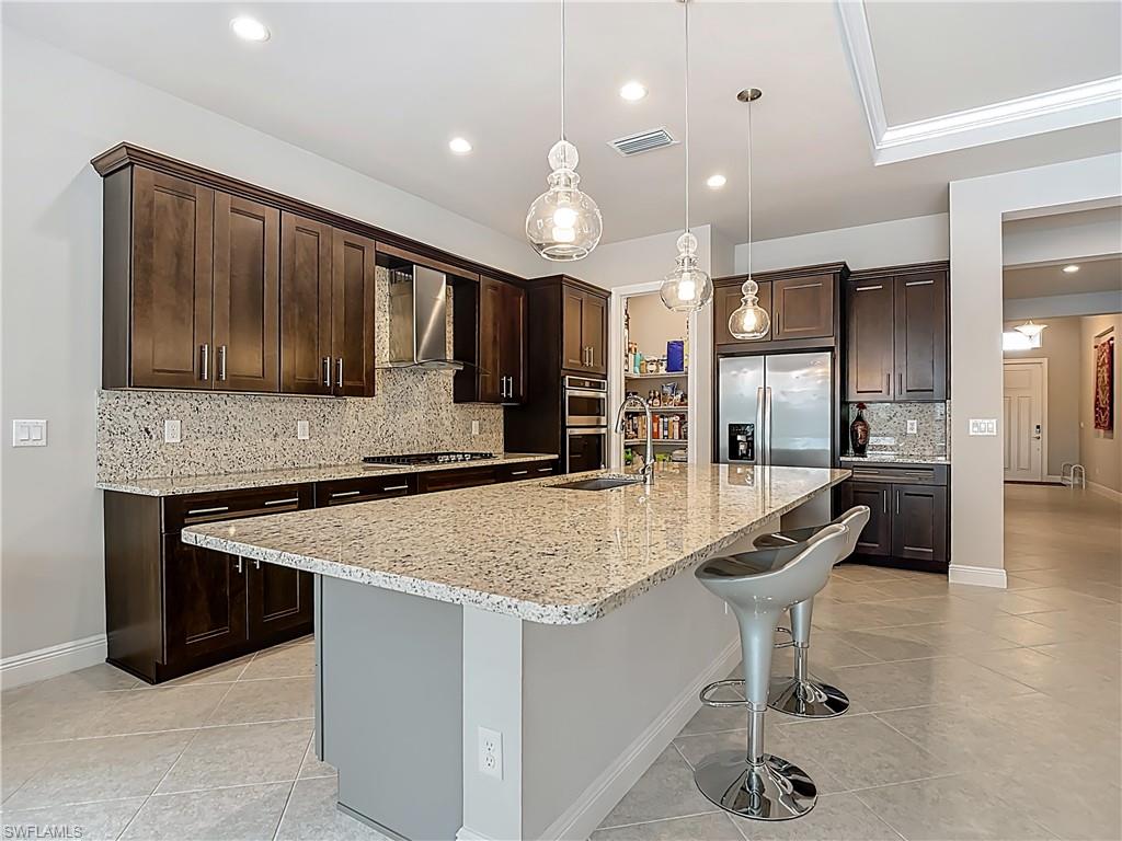 8980 Mustique Lane Naples, FL 34114 - Photo 18 of 50 Kitchen featuring dark brown cabinets, decorative backsplash, a kitchen breakfast bar, pendant lighting, and light stone countertops