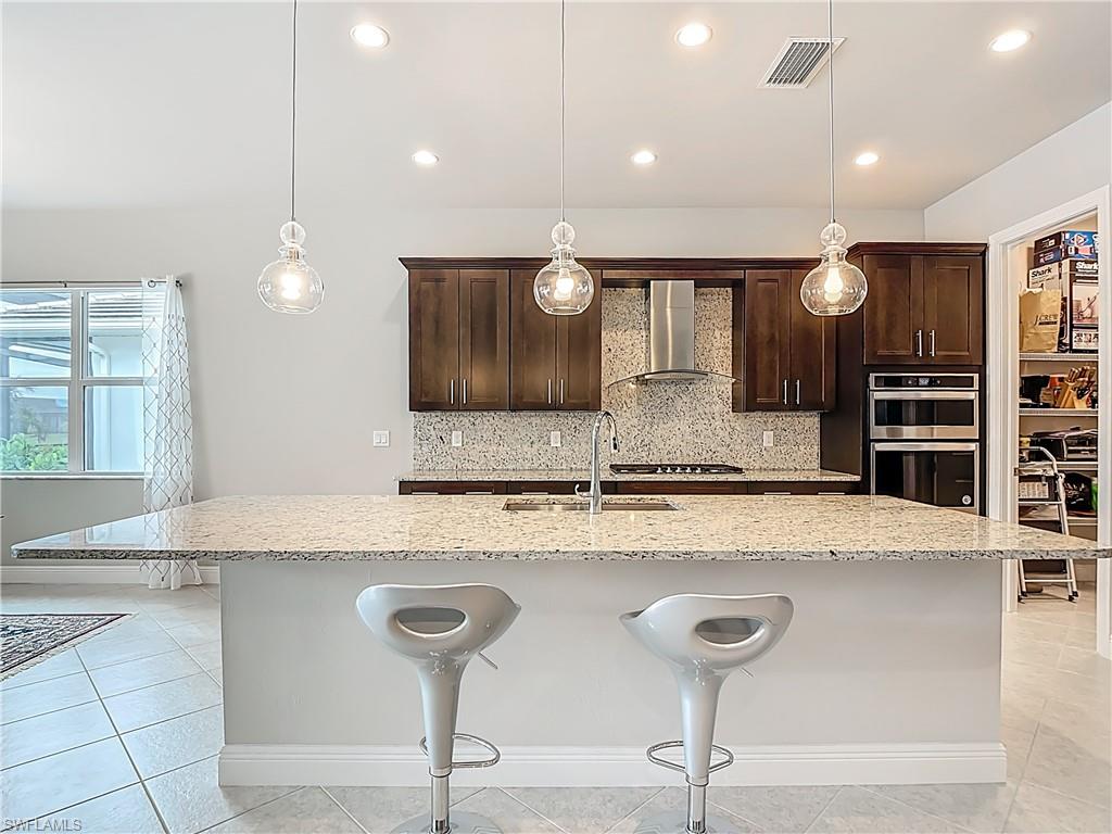 8980 Mustique Lane Naples, FL 34114 - Photo 19 of 50 Kitchen featuring a kitchen breakfast bar, dark brown cabinets, light stone counters, backsplash, and an island with sink