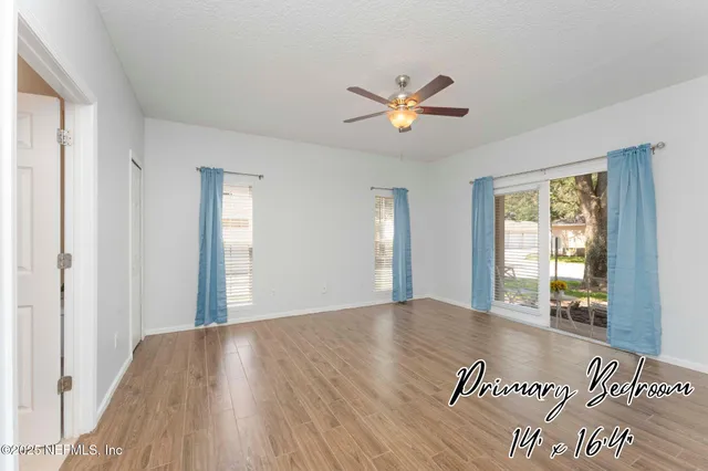 a view of an empty room with wooden floor and a ceiling fan