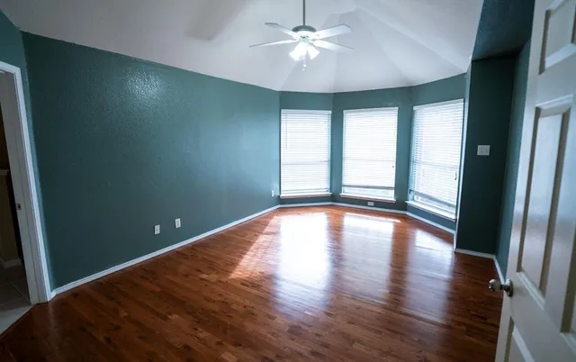 a view of empty room with wooden floor and fan