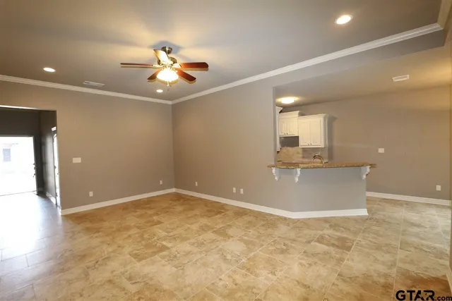 an empty room with kitchen view and a ceiling fan