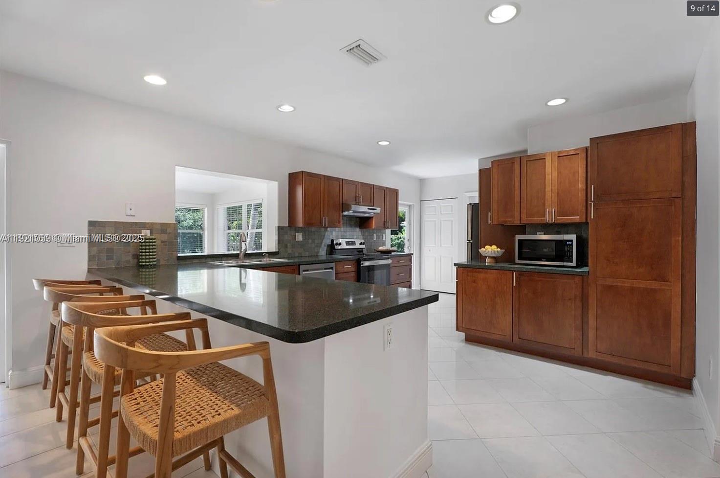 8700 Southwest 64th Avenue Pinecrest, FL 33156 - Photo 9 of 14 a kitchen with kitchen island granite countertop stainless steel appliances a stove top oven a sink and a refrigerator
