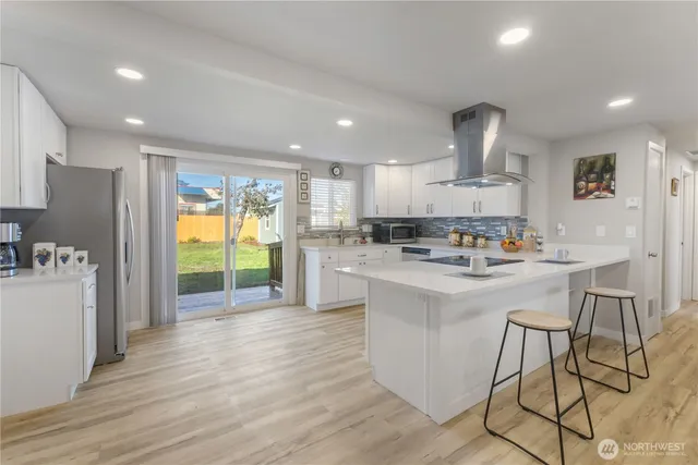 a kitchen with stainless steel appliances a refrigerator a sink dishwasher a stove and a dining table with wooden floor