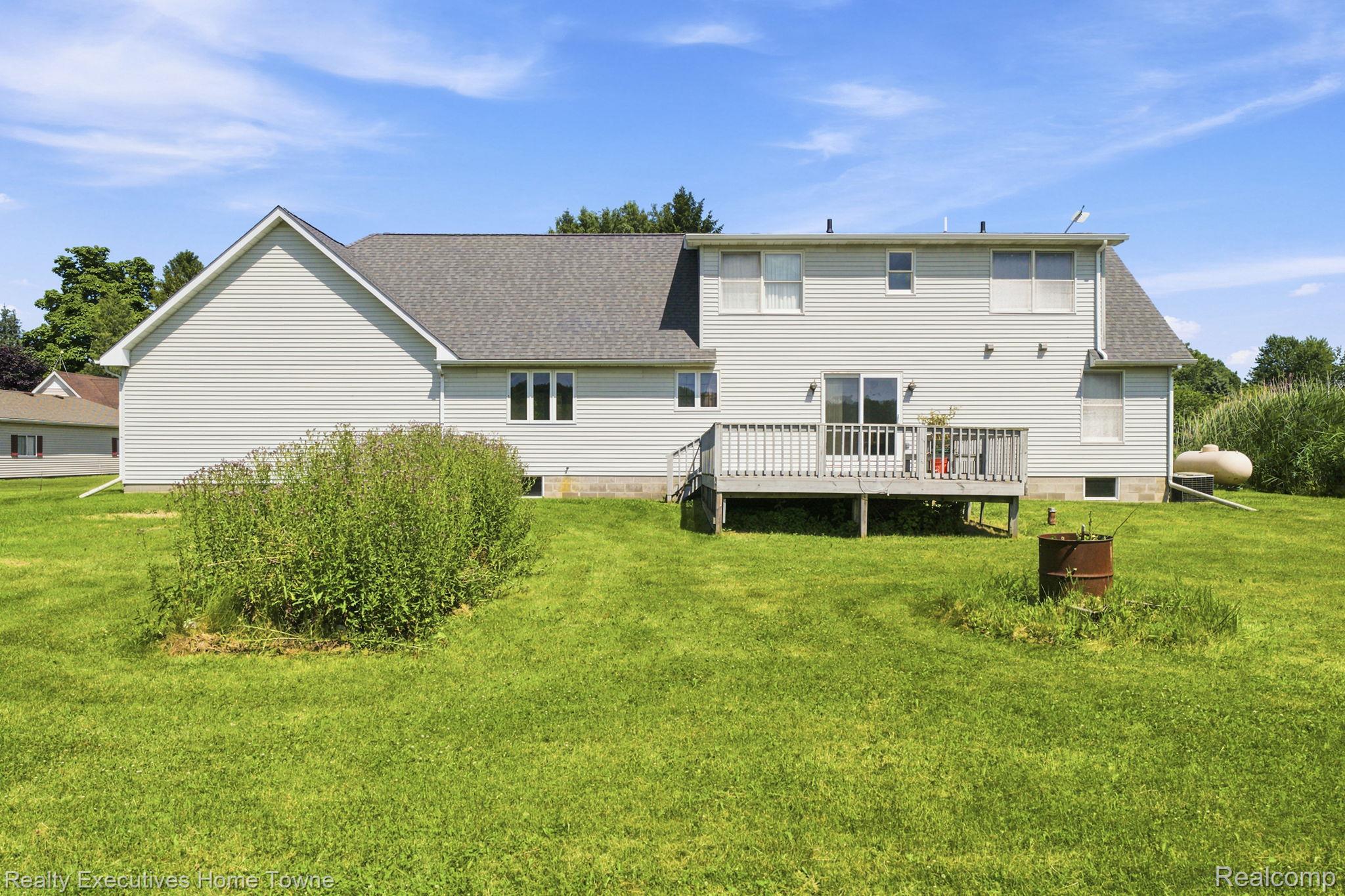959 Braidwood Road Memphis, MI 48041 - Photo 51 of 58 Rear exterior featuring a spacious wooden deck with railings, light-colored siding, a gray shingled roof, sliding glass doors, and multiple windows