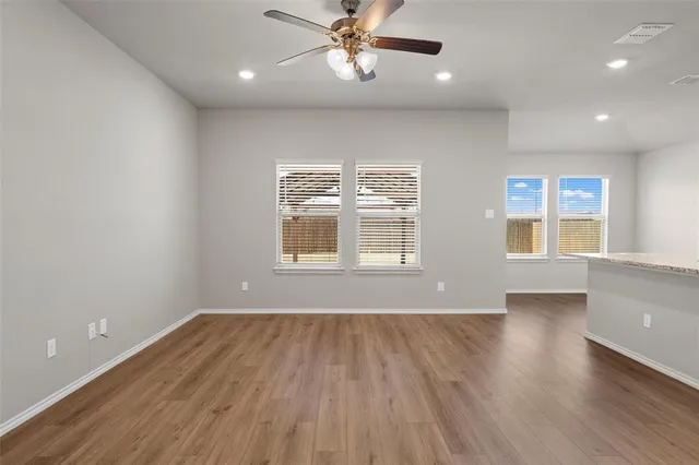 an empty room with wooden floor a ceiling fan and windows