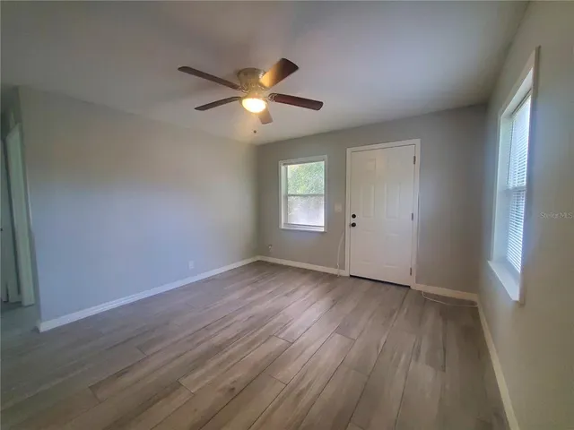 an empty room with wooden floor fan and windows