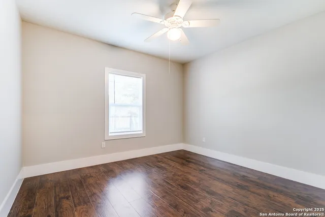 an empty room with wooden floor ceiling fan and windows