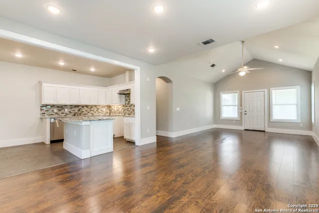 a view of an empty room and kitchen with a sink wooden floor and a large window