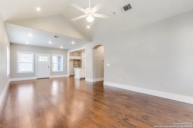 a view of an empty room with wooden floor and a ceiling fan