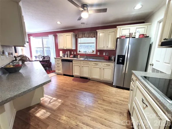a kitchen with stainless steel appliances granite countertop a refrigerator a sink dishwasher a stove and a dining table with wooden floor