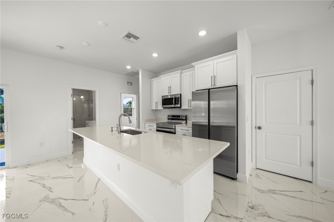 1252 Edna Street East Lehigh Acres, FL 33974 - Photo 8 of 25 a large kitchen with stainless steel appliances kitchen island a large counter top and a refrigerator