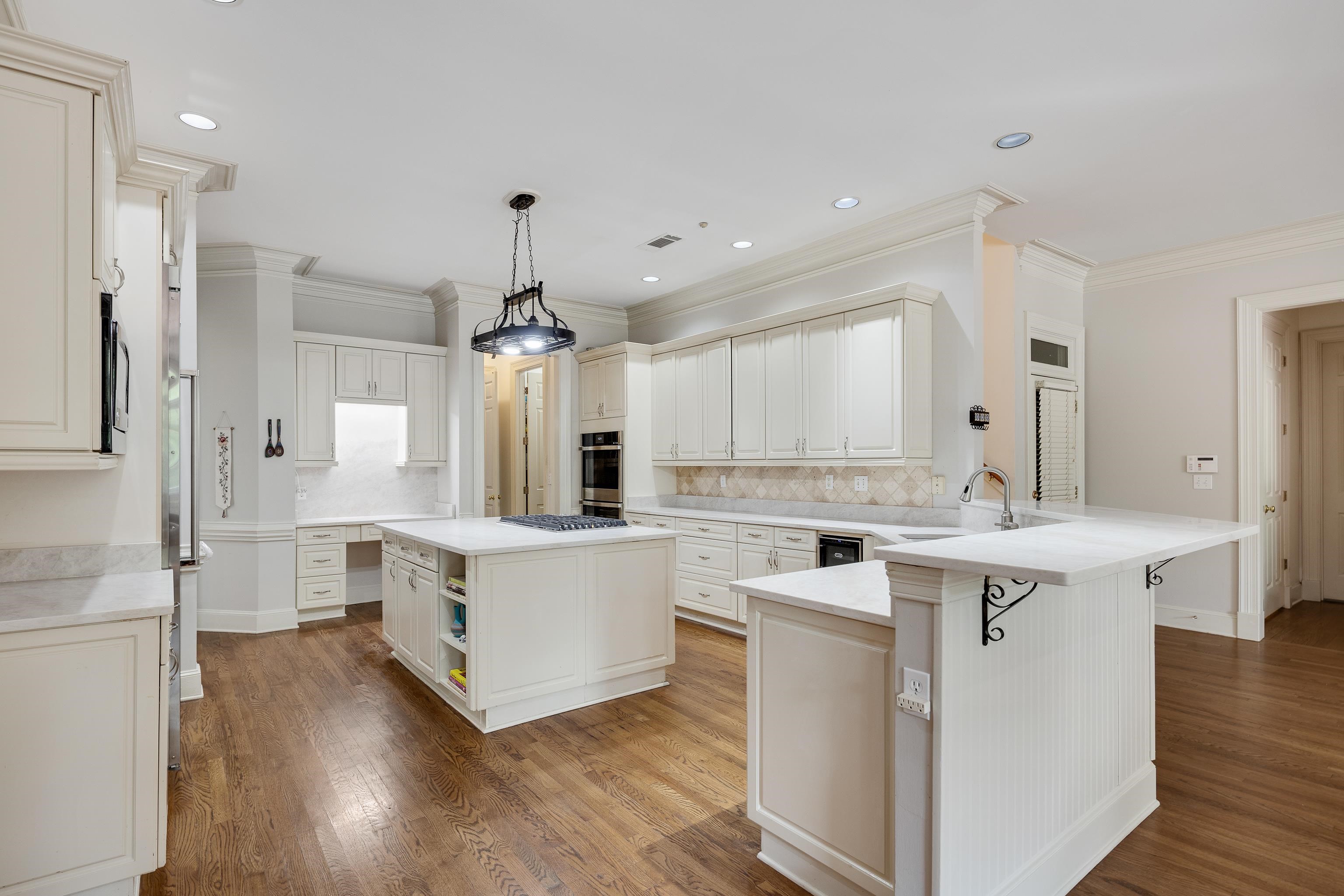 350 Bluff Ridge Cove Memphis, TN 38018 - Photo 16 of 37 Expansive kitchen featuring wood-finish flooring, white cabinetry, integrated appliances, a central island with a cooktop, and a secondary island with a sink and breakfast bar