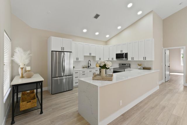 a kitchen with stainless steel appliances granite countertop a refrigerator a sink dishwasher a stove and white countertops with wooden floor