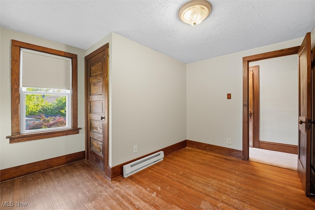 10536 Johnnycake Ridge Road Painesville, OH 44077 - Photo 23 of 40 Spare room featuring a baseboard heating unit, hardwood / wood-style flooring, and a textured ceiling