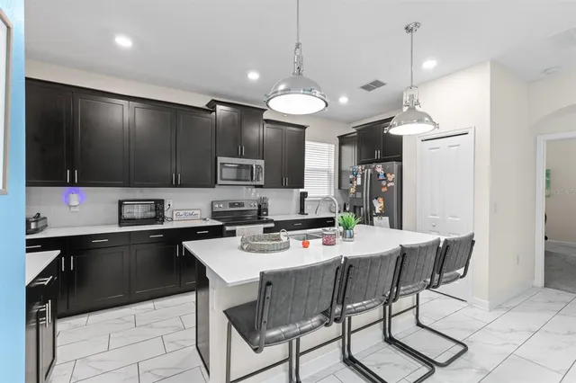 a kitchen with stainless steel appliances kitchen island granite countertop a sink a stove a refrigerator cabinets and chairs