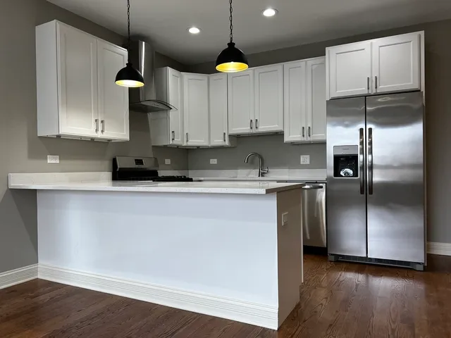 a kitchen with stainless steel appliances granite countertop a refrigerator a sink a stove and white cabinets with wooden floors