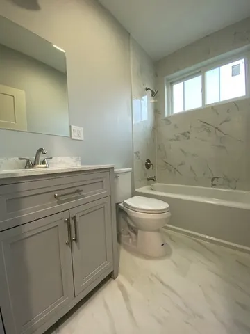 a bathroom with a granite countertop toilet a sink a mirror and a bathtub