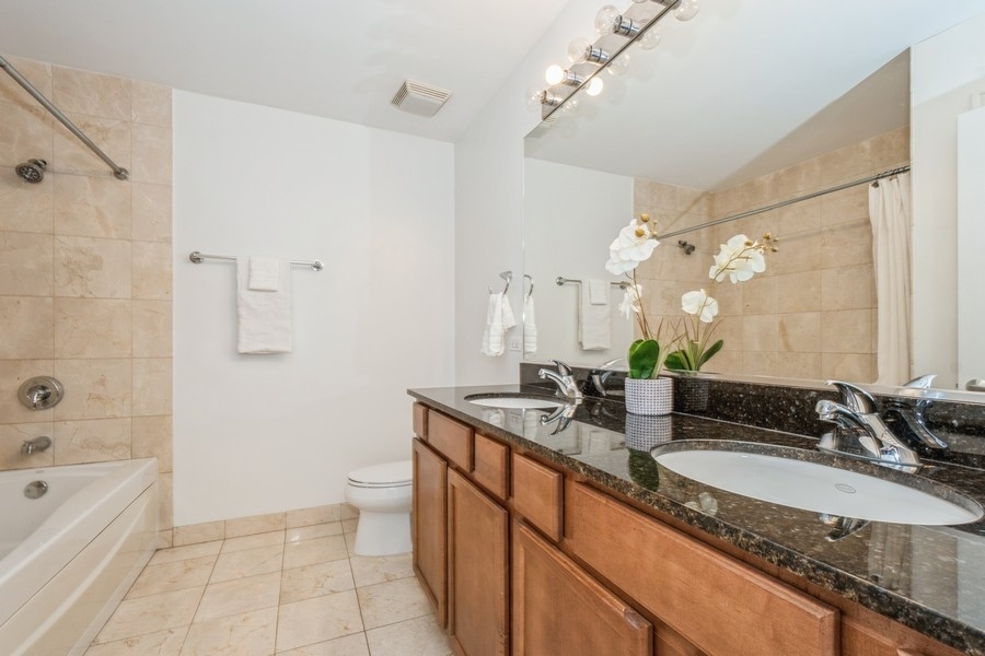4814 North Clark Street, Unit 201 Chicago, IL 60640 - Photo 18 of 24 a bathroom with a granite countertop sink a mirror a bathtub and shower