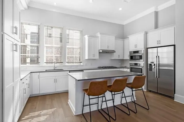 a kitchen with stainless steel appliances granite countertop a stove a sink a refrigerator and white cabinets with wooden floor