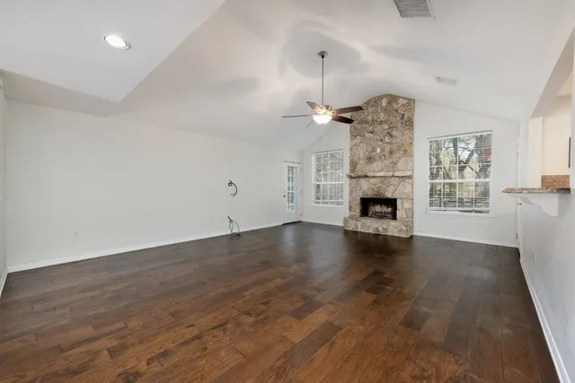 an empty room with wooden floor fireplace and windows
