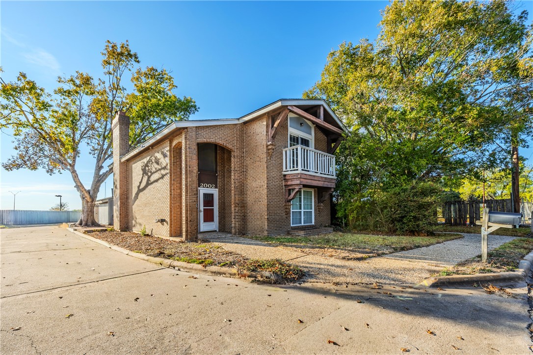 View of front of house with brick siding, a balcony, and a chimney