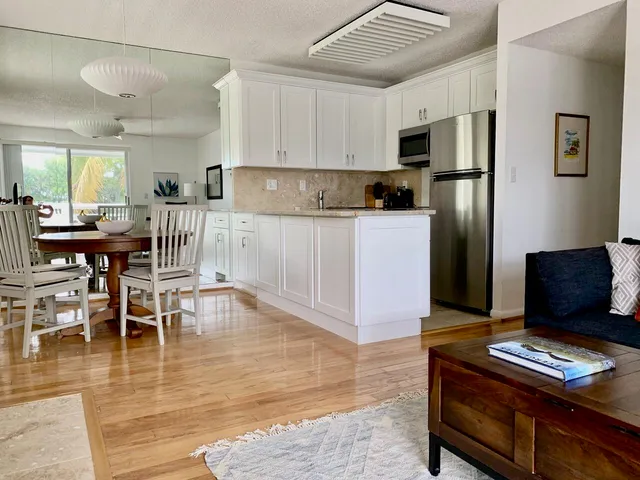 a kitchen with stainless steel appliances kitchen island granite countertop a refrigerator a stove a microwave oven with white cabinets and wooden floor