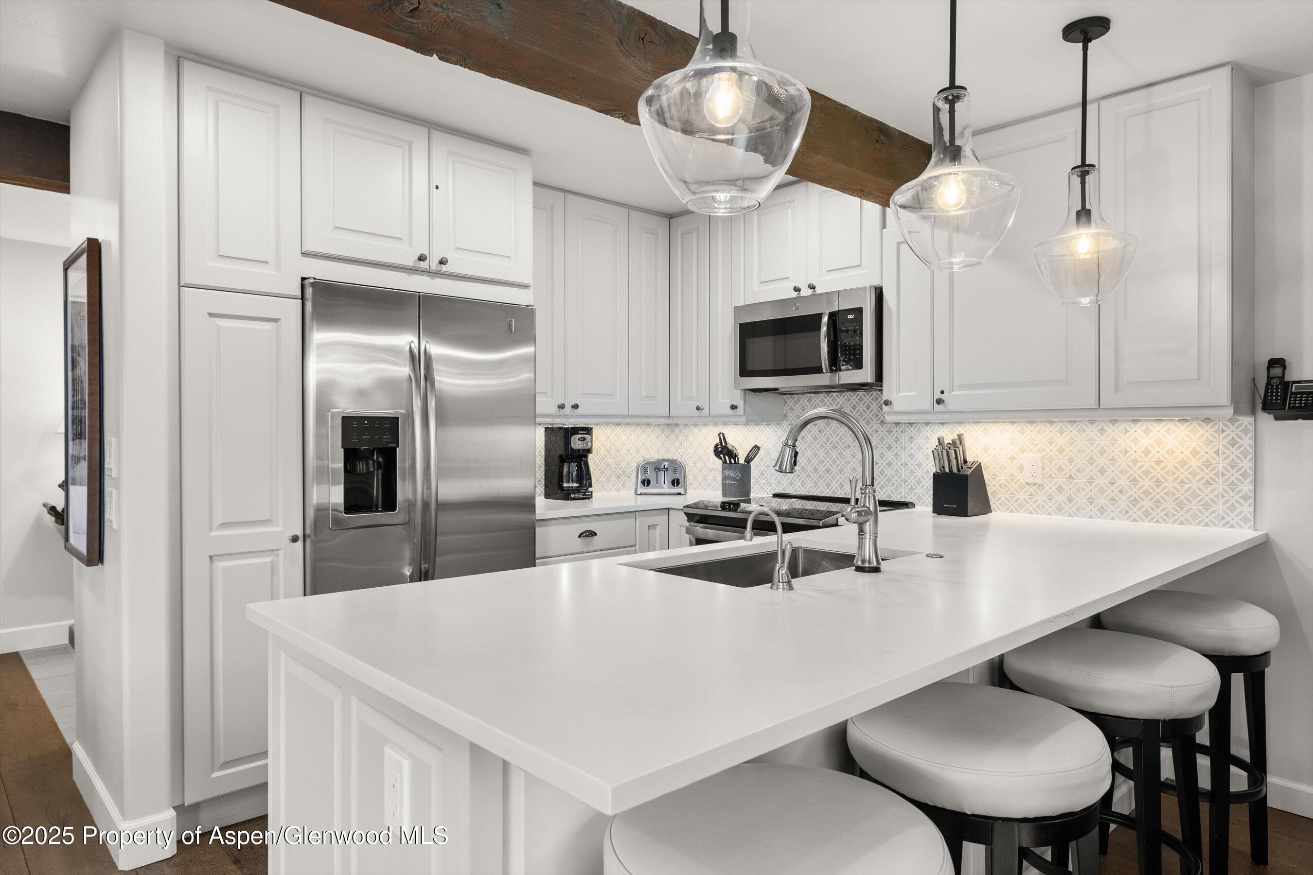 855 Carriage Way, Unit 103 Snowmass Village, CO 81615 - Photo 7 of 26 a kitchen with stainless steel appliances granite countertop a sink a microwave oven a refrigerator a stove and white cabinets with wooden floor