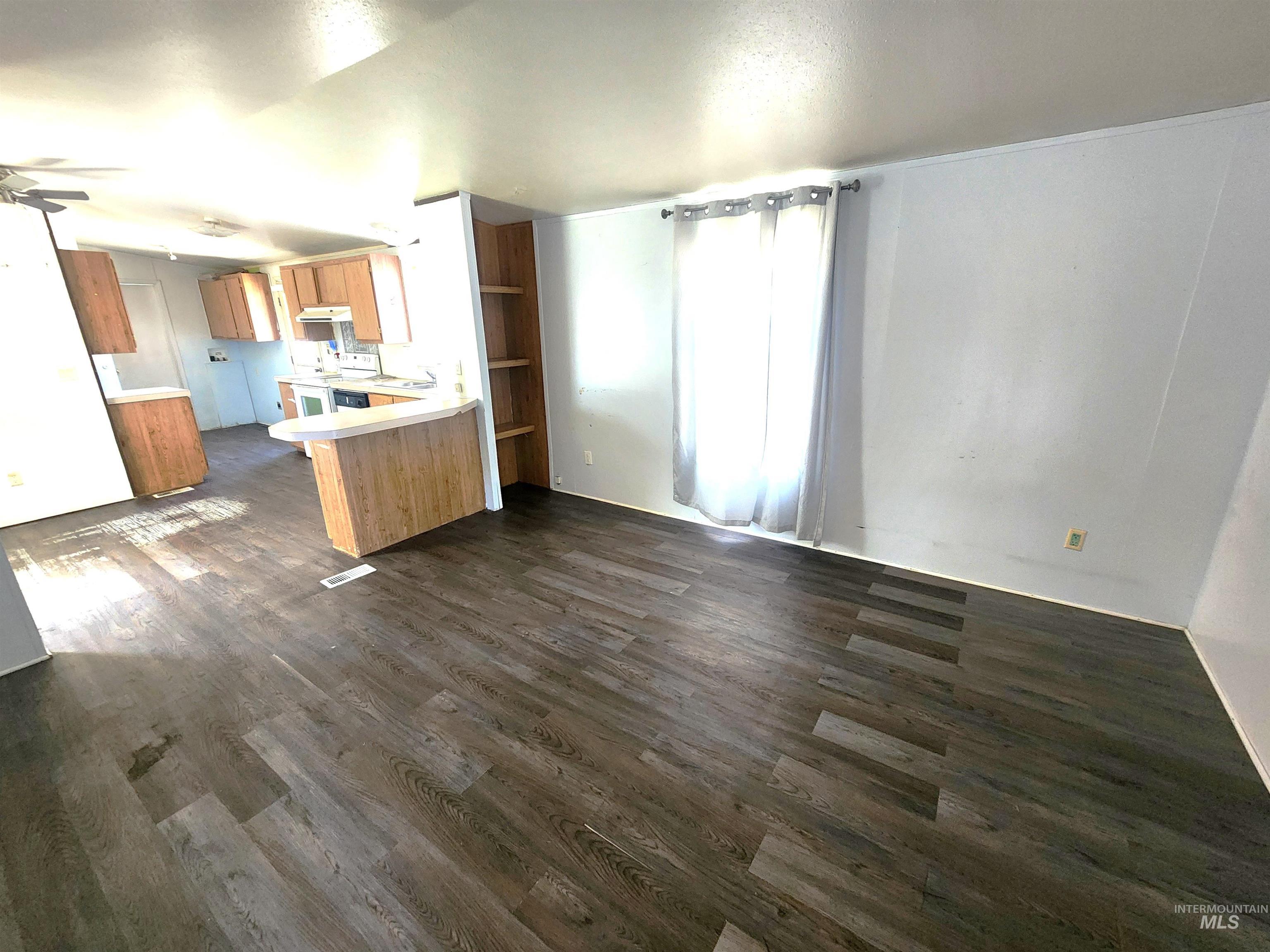 616 North Kings Road Nampa, ID 83687 - Photo 2 of 12 Open-concept living area featuring wood-finish flooring, a ceiling fan, and a kitchen with wood cabinetry and a curved breakfast bar