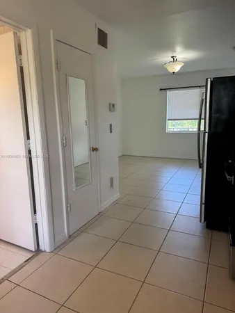 a view of a refrigerator in kitchen and an empty room in wooden floor