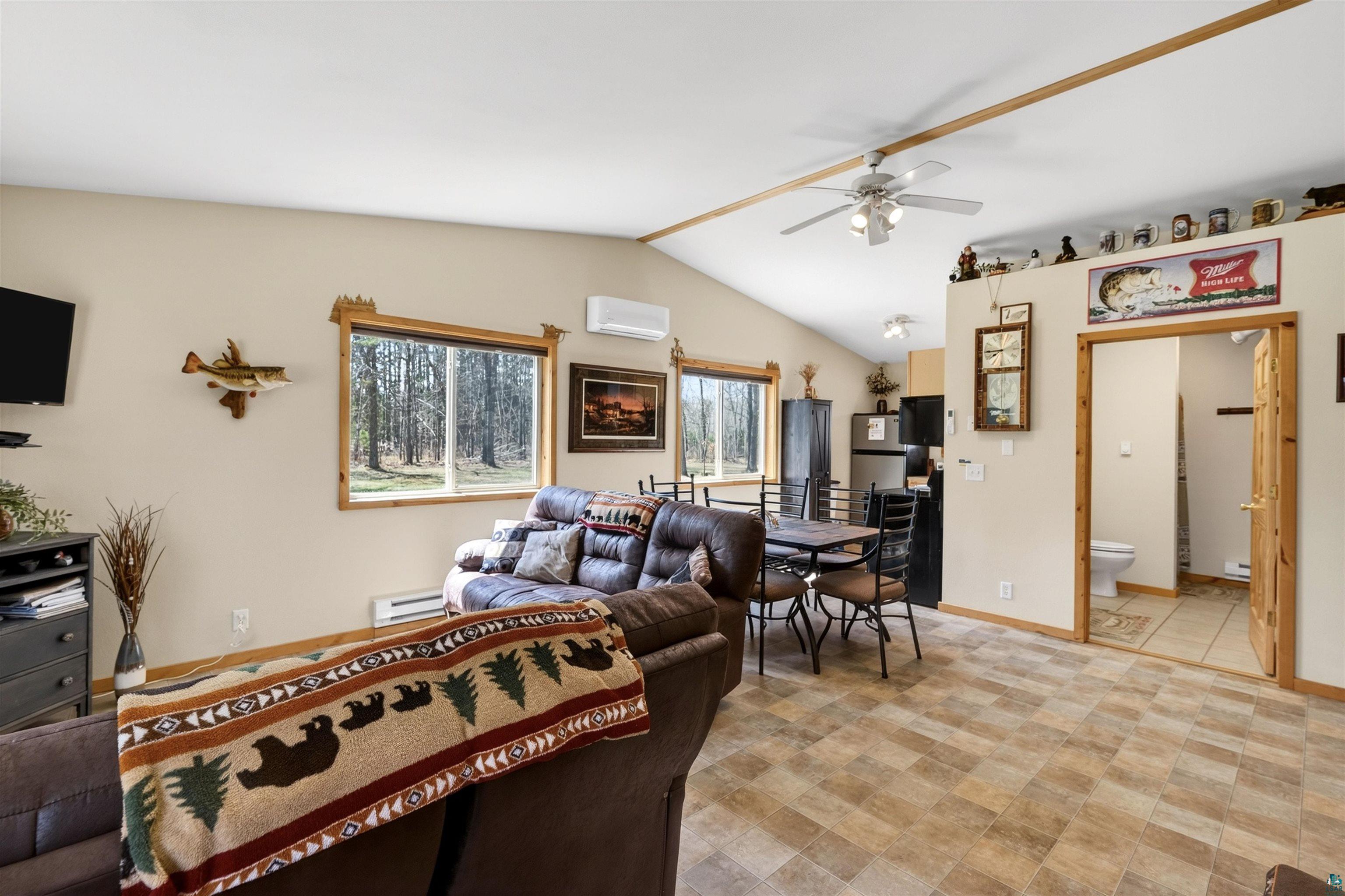 12235 East Crooked Lake Road Gordon, WI 54838 - Photo 7 of 48 Vaulted ceiling with a ceiling fan, wood-finish flooring, two large windows with natural wood trim, and a wall-mounted mini-split AC unit