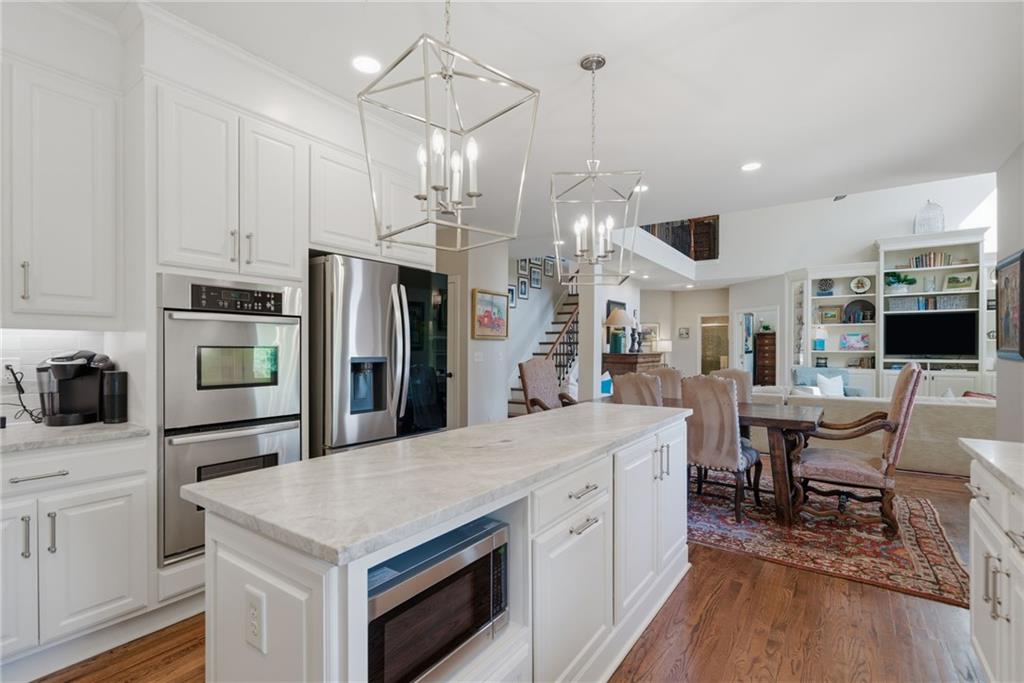 535 Brayford Way Suwanee, GA 30024 - Photo 19 of 55 a open kitchen with stainless steel appliances kitchen island granite countertop a refrigerator a stove a sink a dining table and chairs with wooden floor