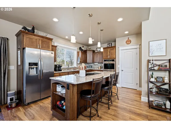 a kitchen with stainless steel appliances kitchen island granite countertop a refrigerator a stove a sink a dining table and chairs with wooden floor
