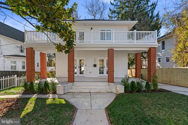 a view of a white house with a large windows and a yard with plants and large tree