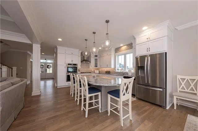 a kitchen with stainless steel appliances kitchen island granite countertop a refrigerator a stove a sink a dining table and chairs with wooden floor
